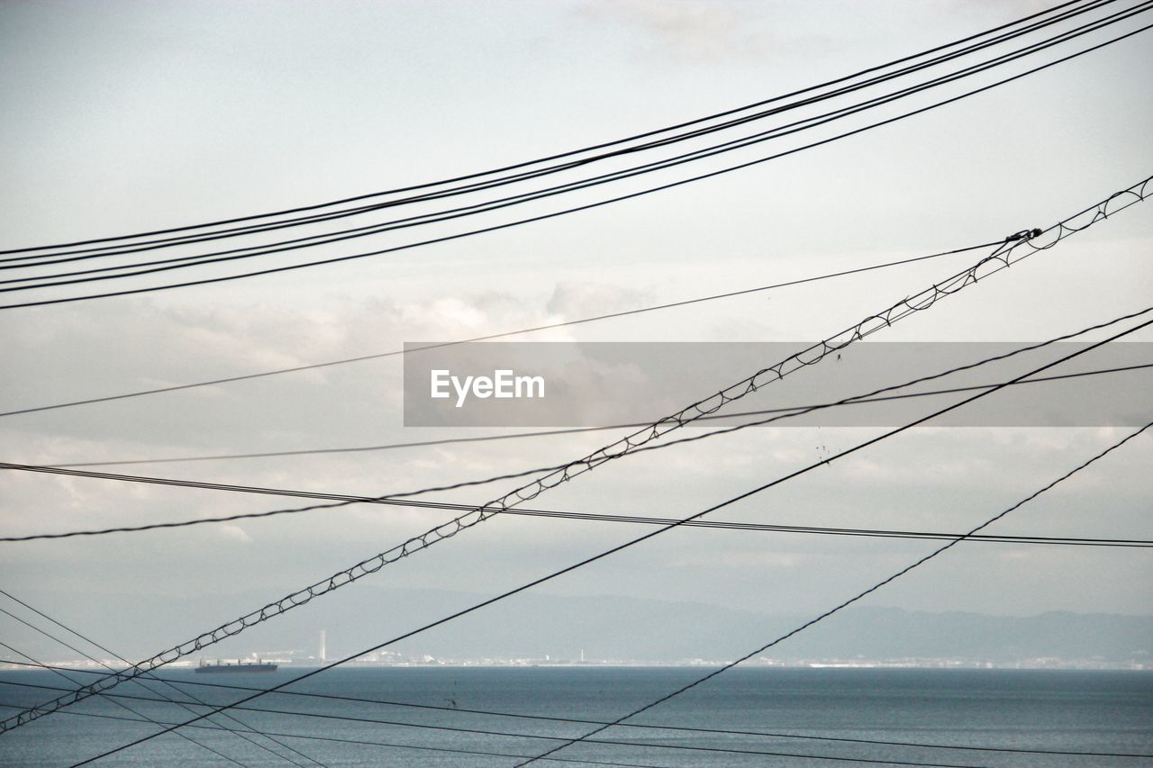 Low angle view of tangled cables over sea against cloudy sky