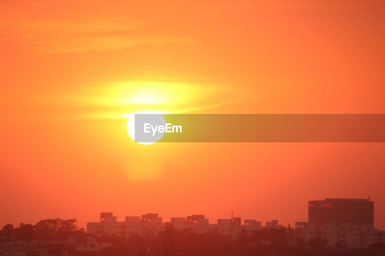 sky, horizon, sunset, afterglow, city, architecture, building exterior, built structure, cityscape, sun, urban skyline, dawn, orange color, landscape, building, nature, sunlight, beauty in nature, no people, red sky at morning, dramatic sky, skyscraper, office building exterior, scenics - nature, residential district, silhouette, outdoors, city life, astronomical object, cloud, environment, travel destinations, evening, orange, tranquility, yellow, romantic sky, copy space, idyllic, skyline, haze, vibrant color, sunbeam, travel, tranquil scene