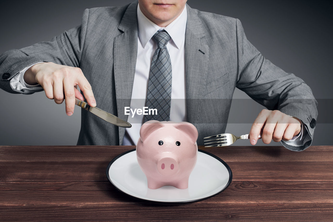 midsection of man holding piggy bank on table