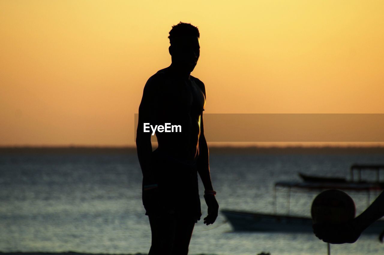 REAR VIEW OF SILHOUETTE MAN STANDING ON BEACH AGAINST SKY