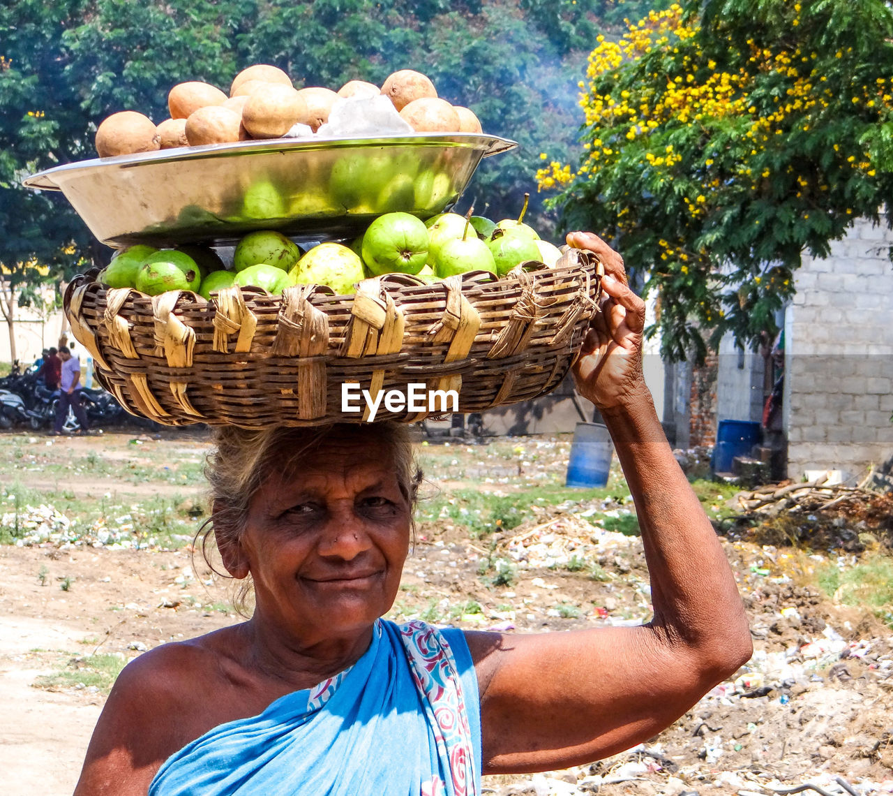 Portrait of smiling senior woman carrying fruits in basket in city