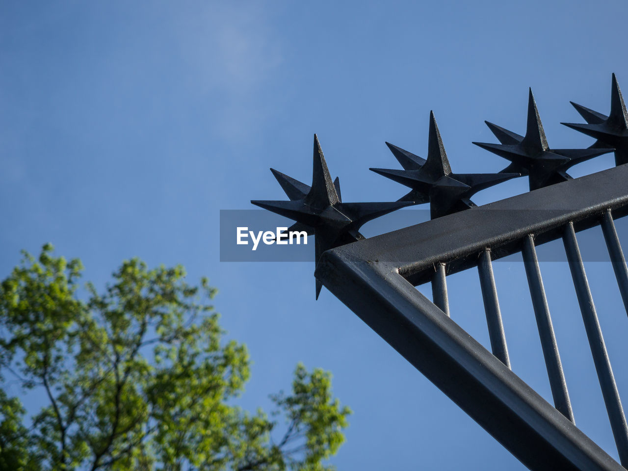 Low angle view of spiked stars on metal fence against clear blue sky