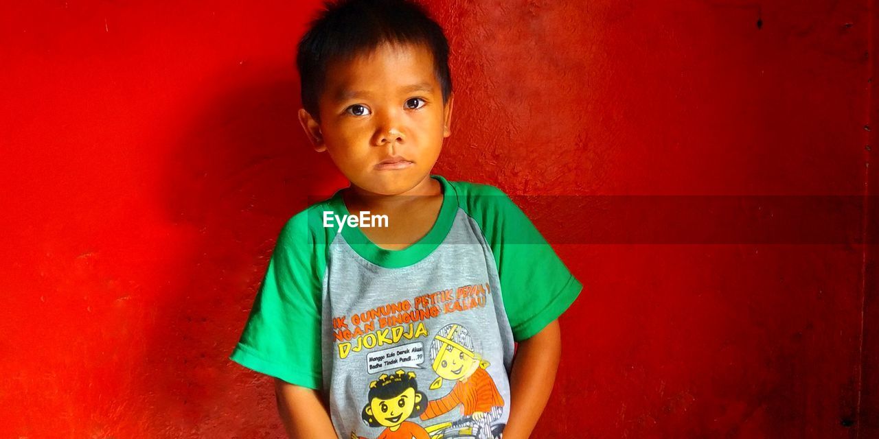 Portrait of boy standing against red wall