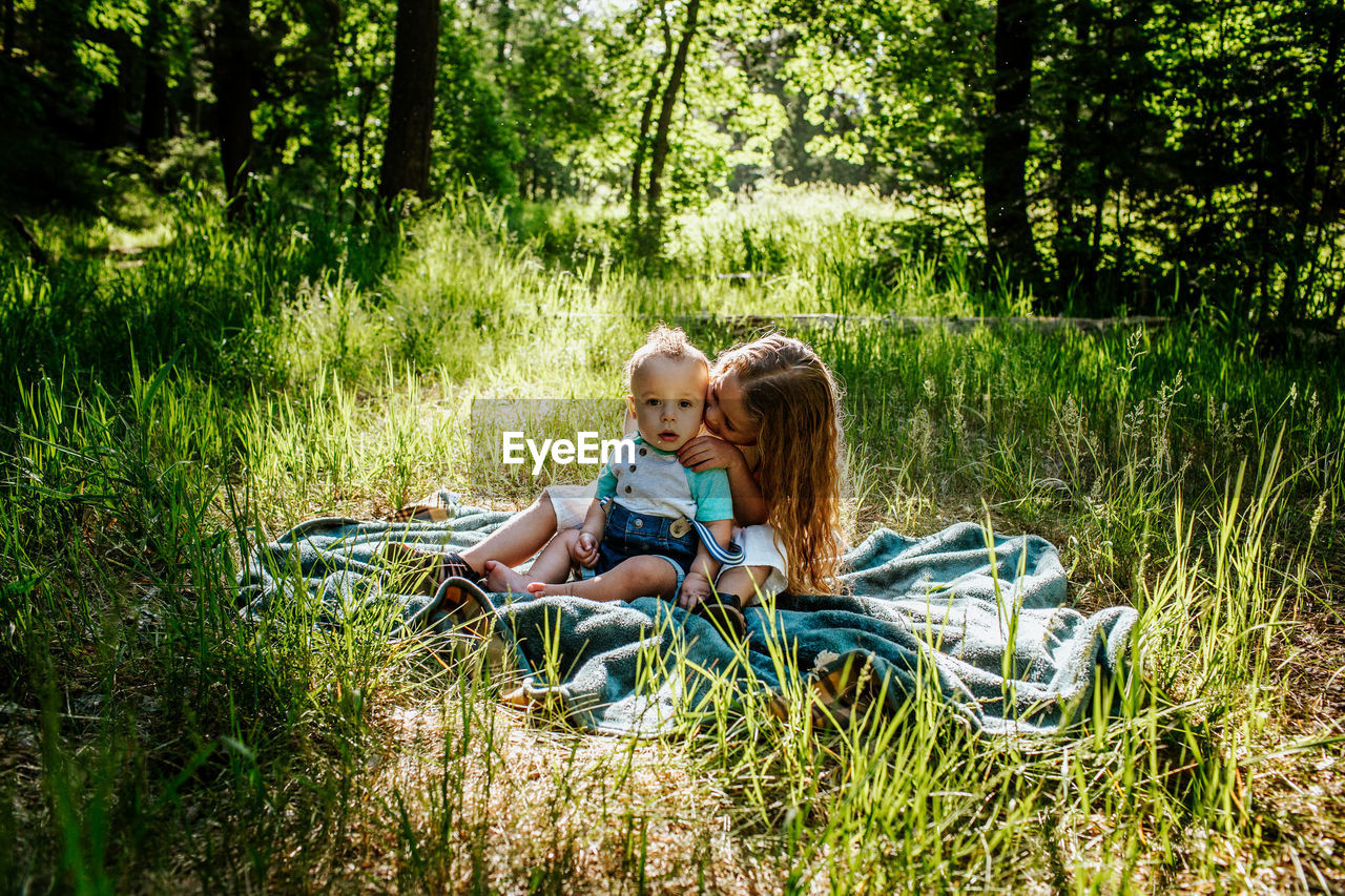 Sister kissing infant brother outside in tall grass