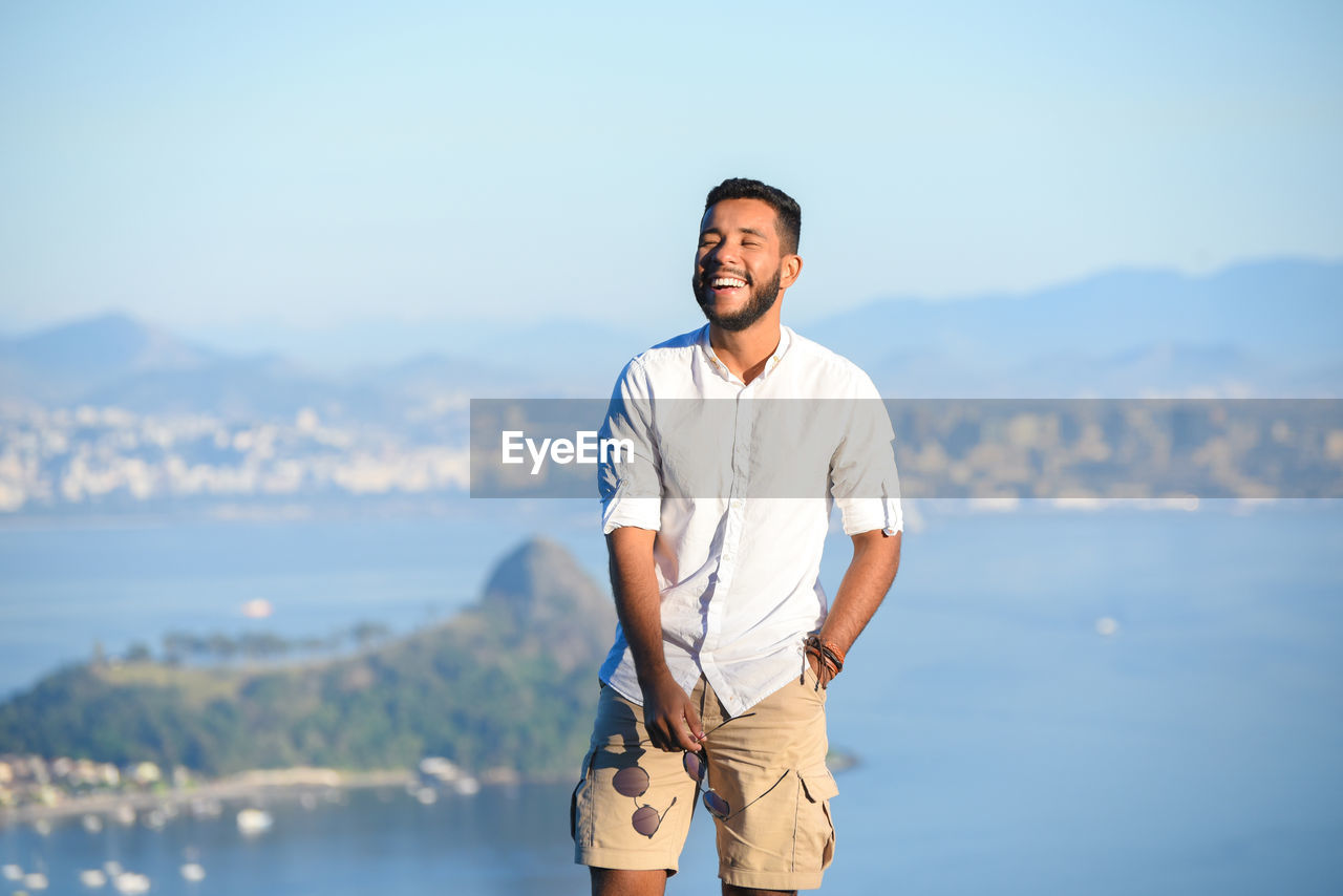 Smiling young man standing against sea