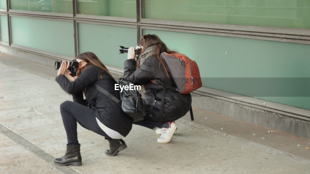 Women photographing through camera on sidewalk
