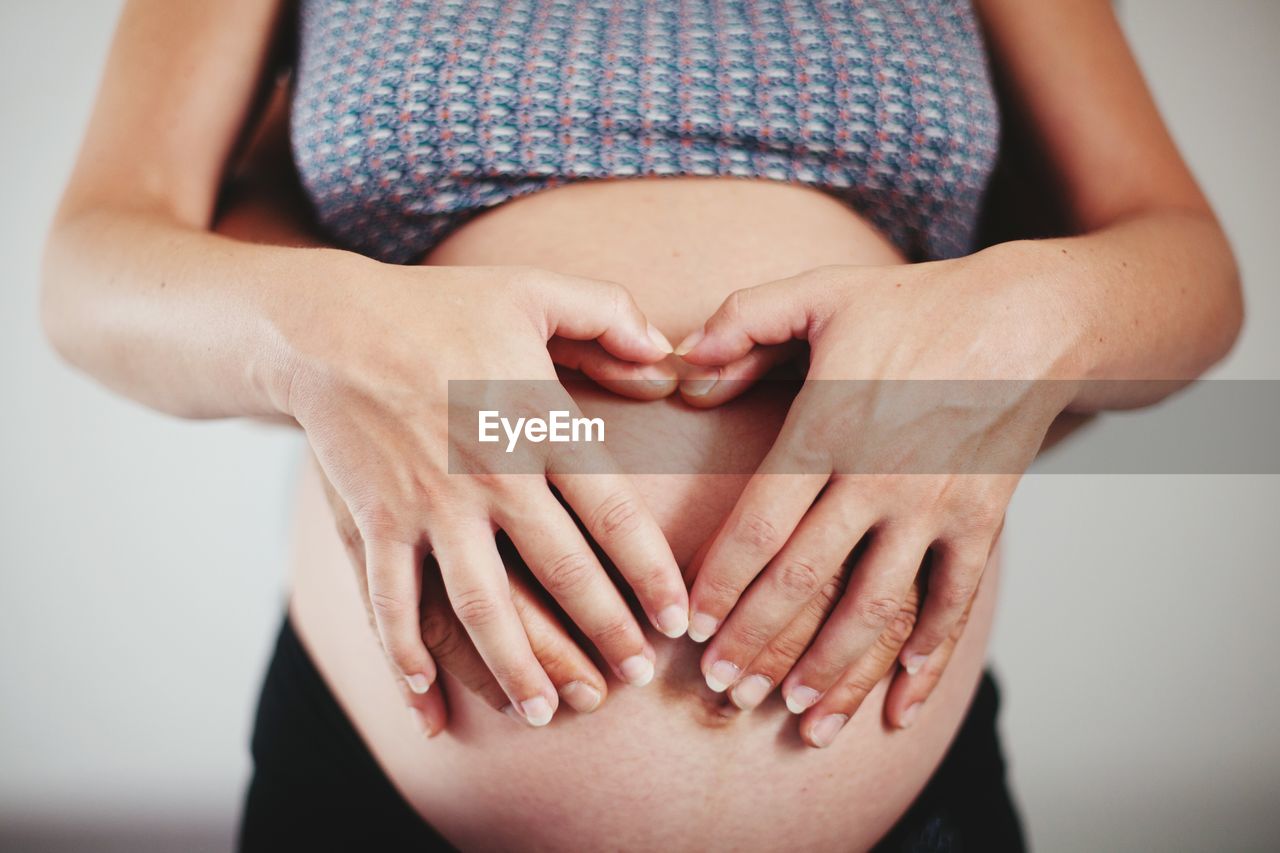 Pregnant woman and husband making heart with hands over abdomen against white background