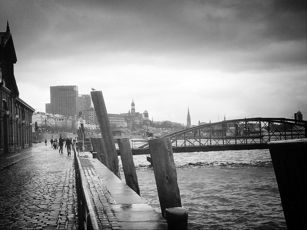 Bridge over river with people walking on cobblestone pathway