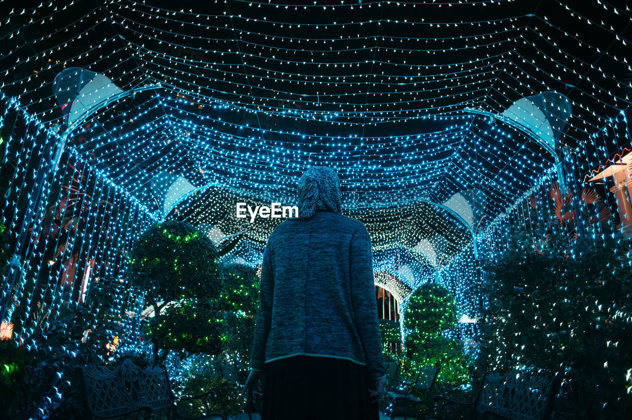 Low angle view of person standing against illuminated lights at night