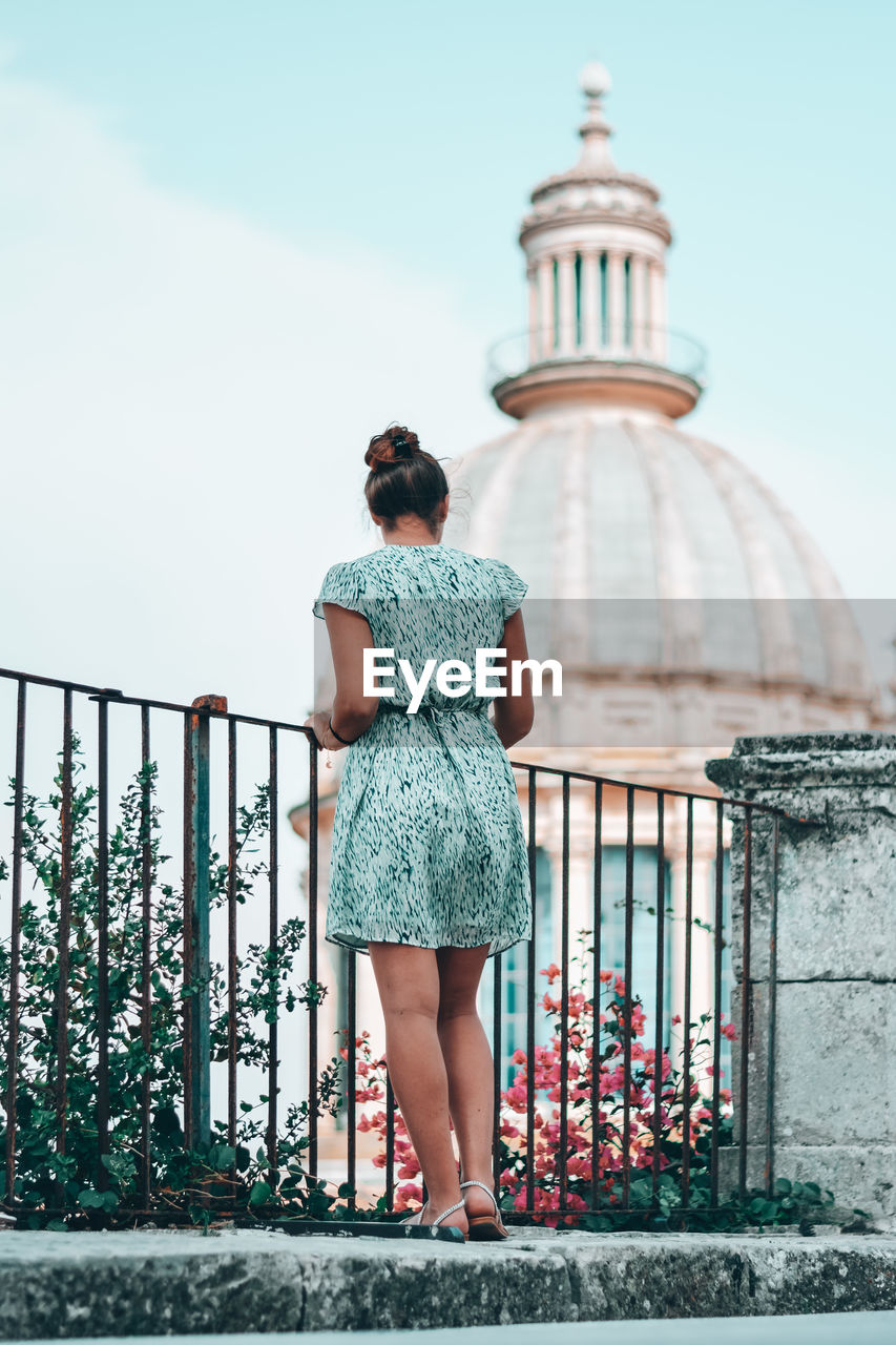 FULL LENGTH REAR VIEW OF WOMAN STANDING AGAINST RAILING