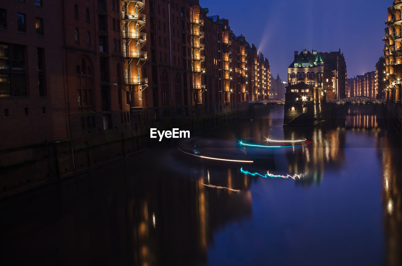 Canal amidst buildings at speicherstadt during night