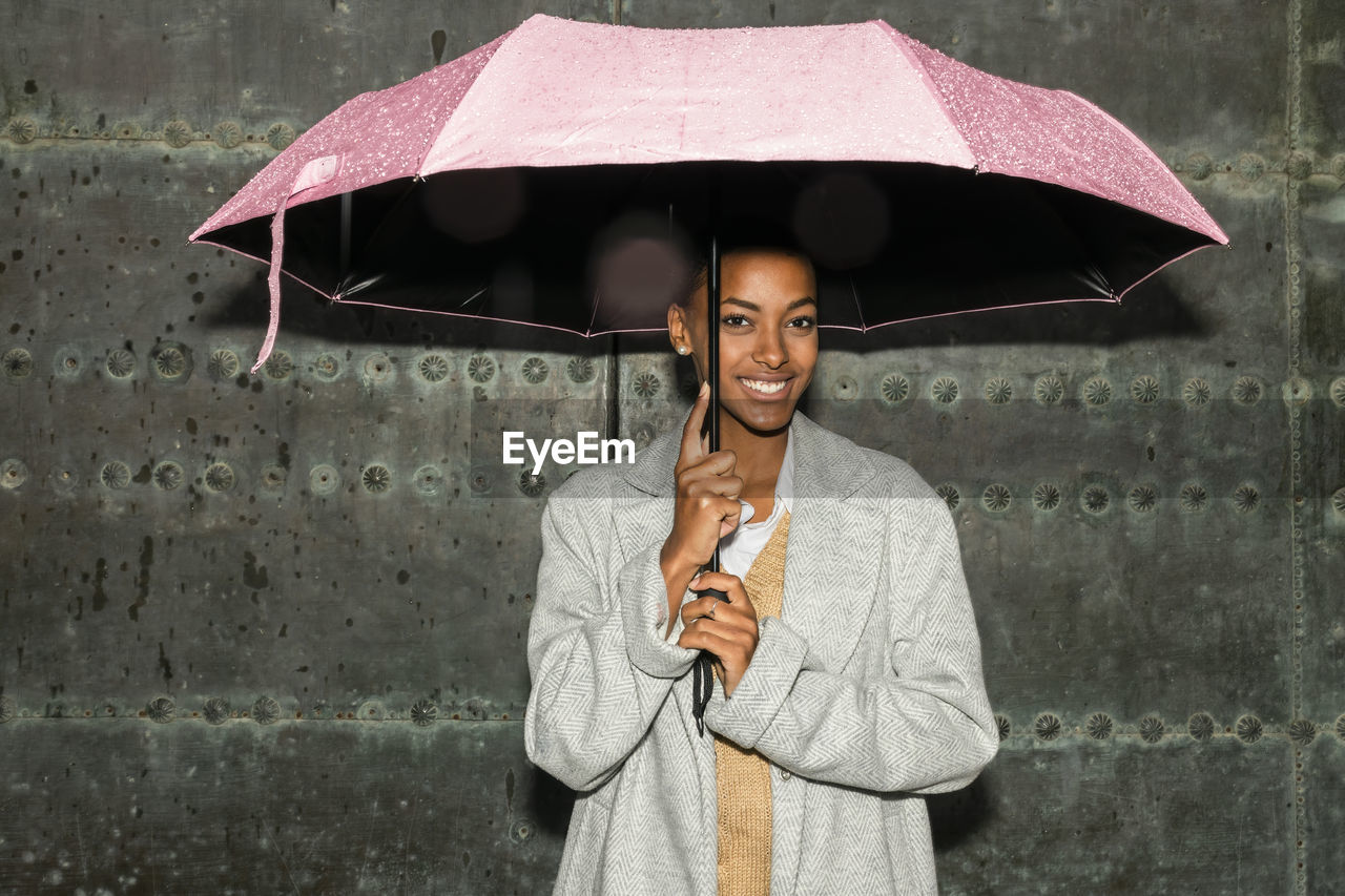 Teenage girl with umbrella standing in front of black wall