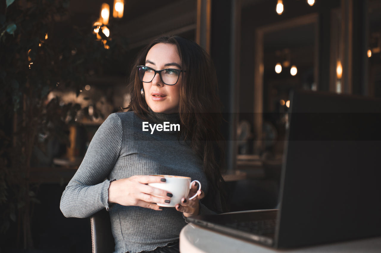 Smiling woman holding coffee sitting in cafe