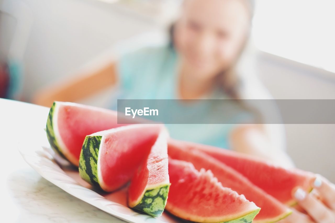 Defocused image of woman sitting in front of watermelon slices in plate on table