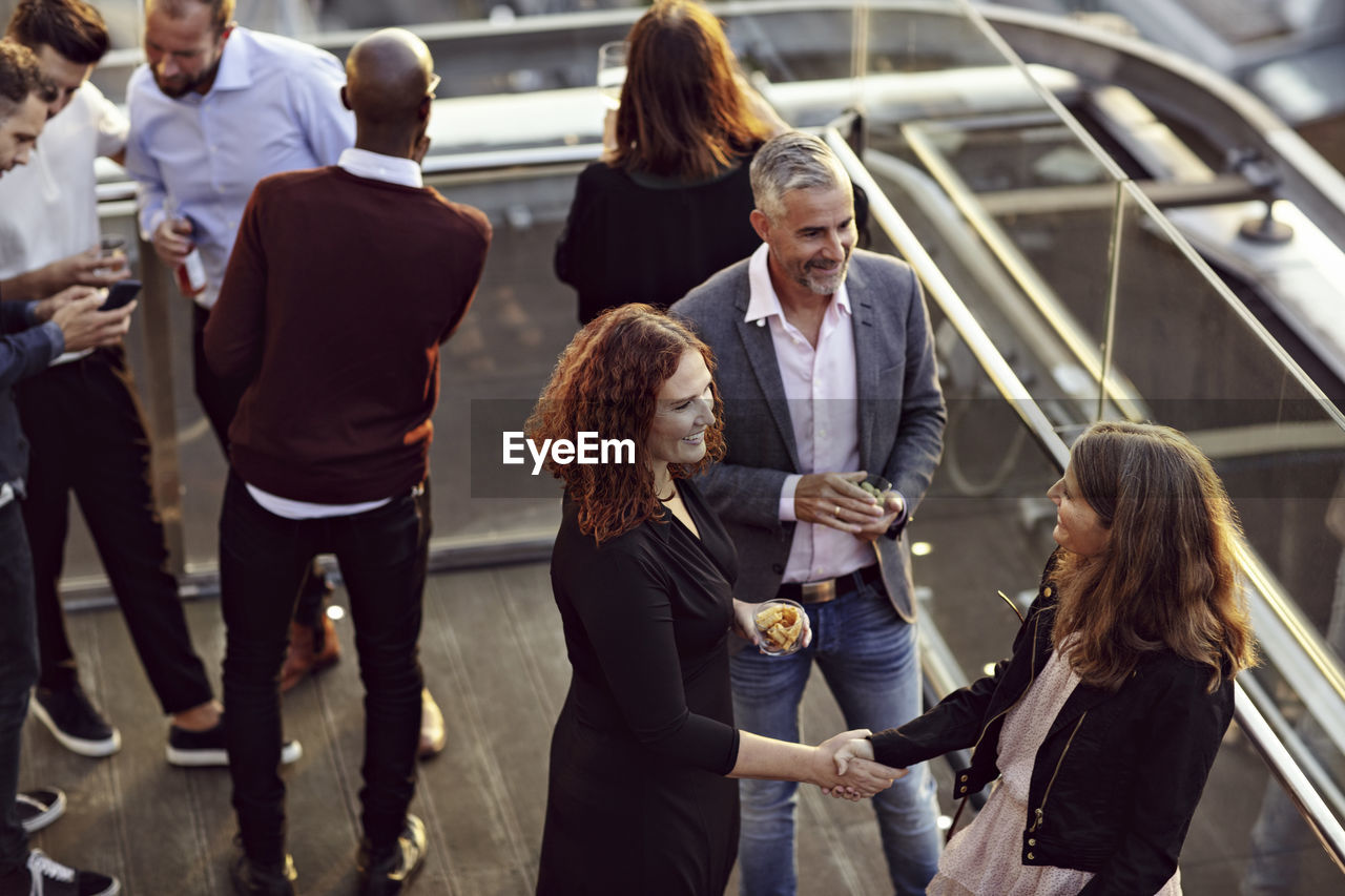 High angle view of businesswoman doing handshake and greeting while partying with coworkers after work on terrace