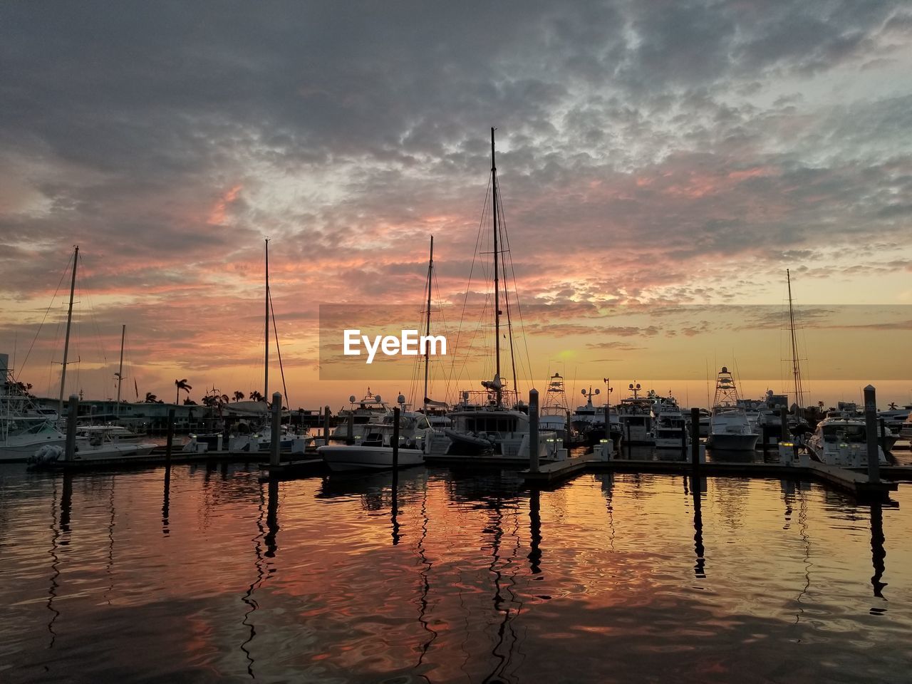 Sailboats moored at harbor during sunset