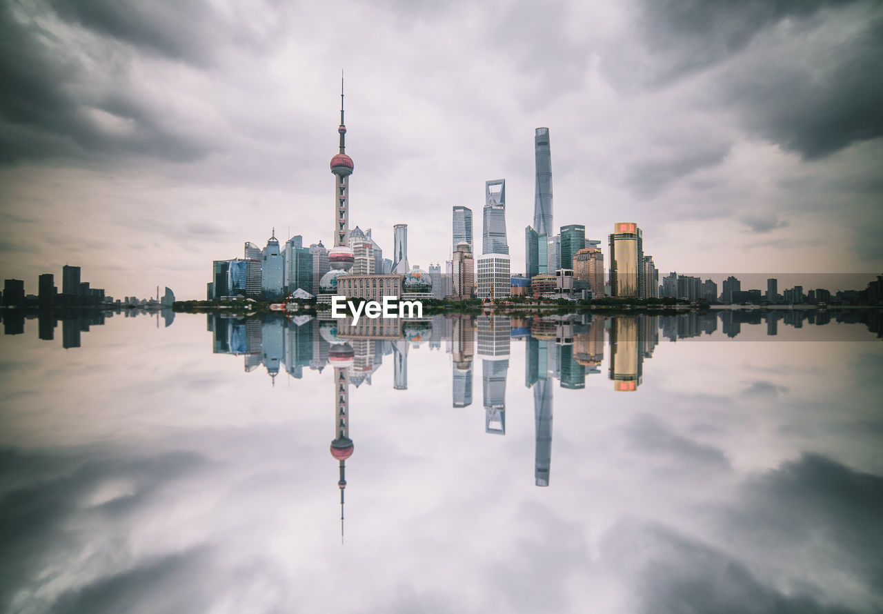 Modern buildings against cloudy sky reflecting on river in city