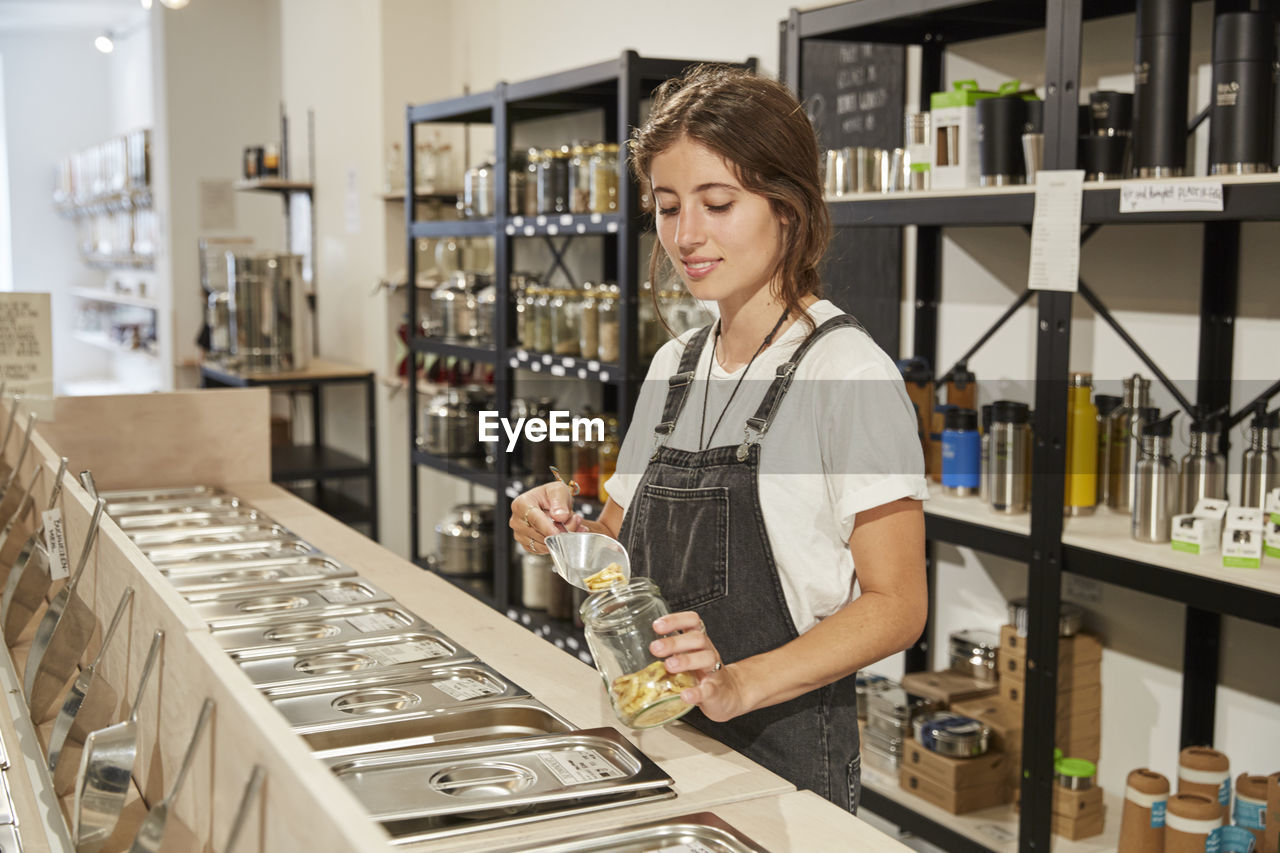 Young woman in packaging-free supermarket filling pasta into jar