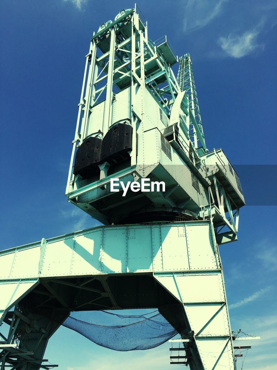 Low angle view of container crane against sky on sunny day