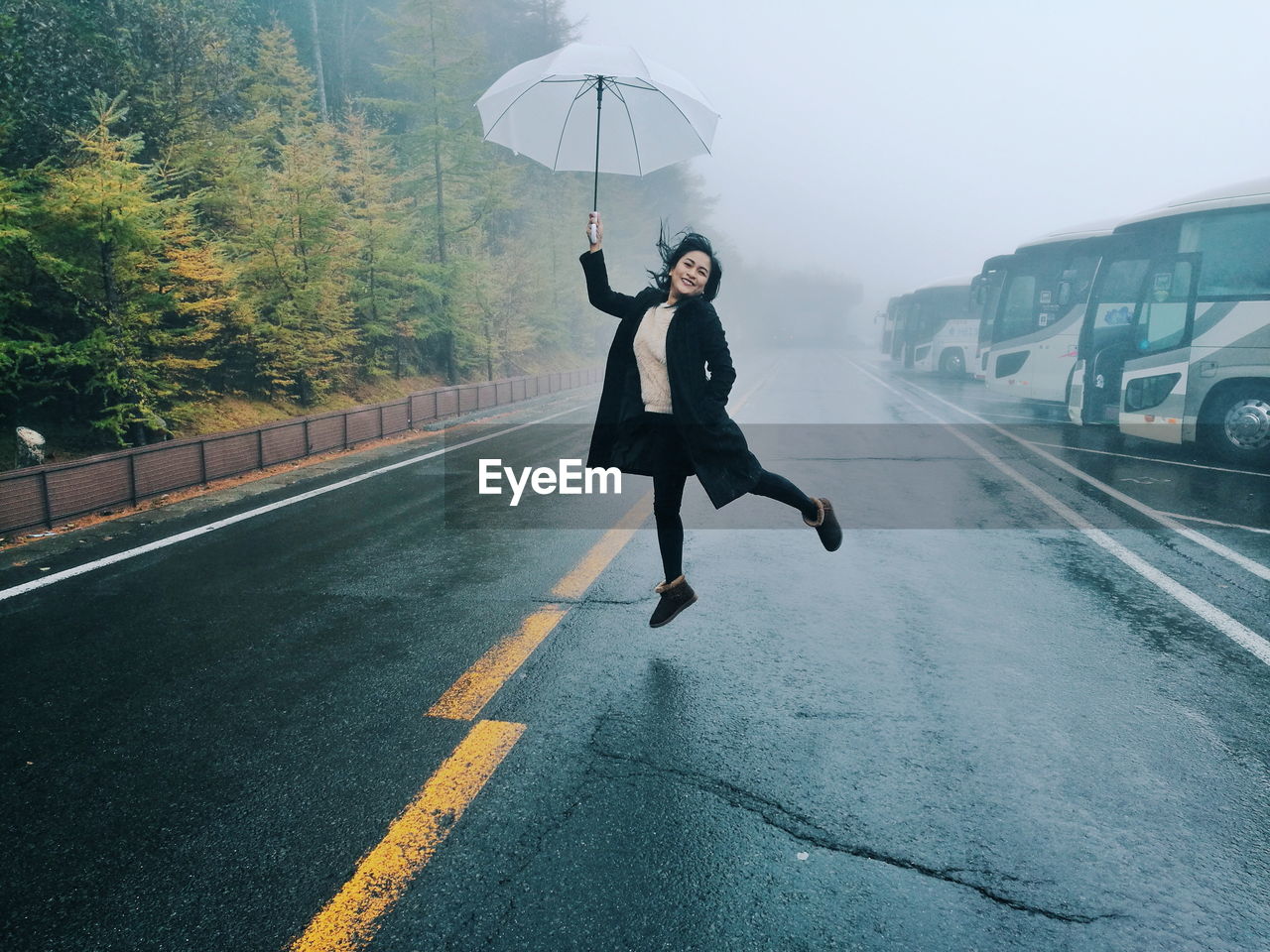 Full length of woman jumping with umbrella on road