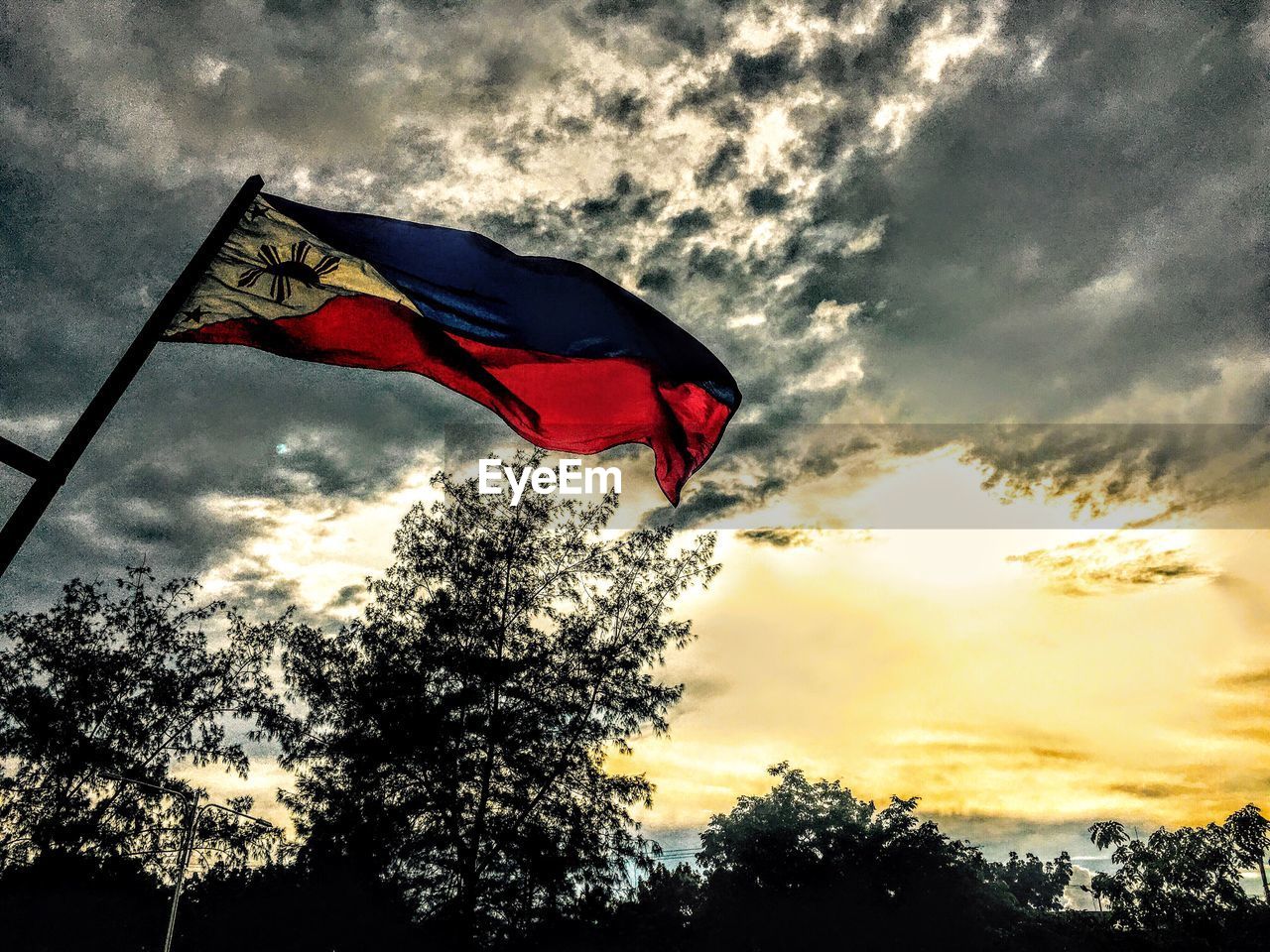 Low angle view of philippines flag by silhouette trees against sky during sunset