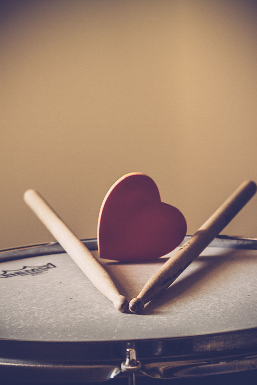 Close-up of heart shape and sticks on drum against wall