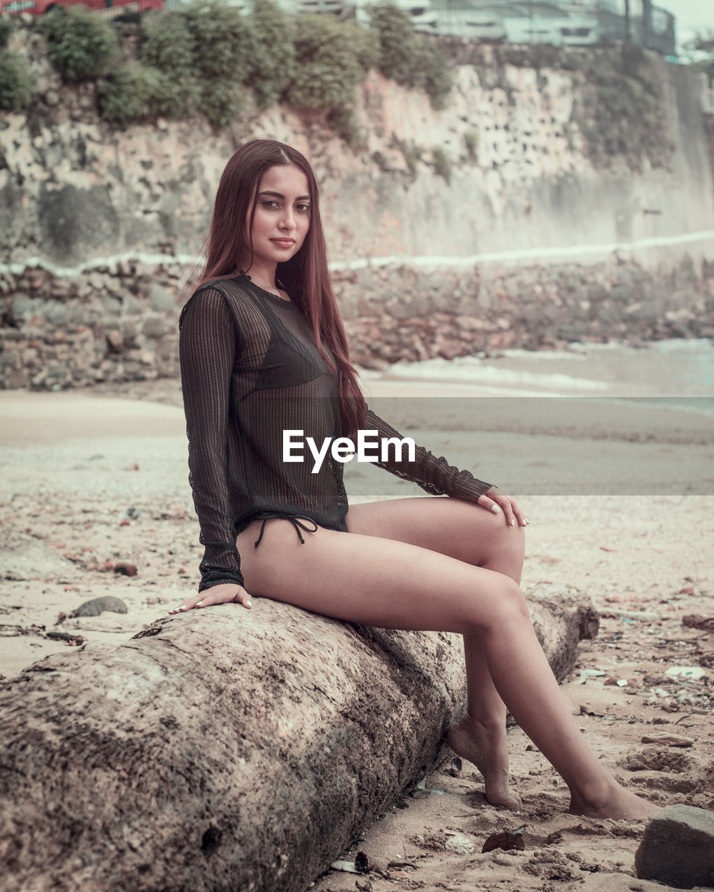 Side view portrait of seductive woman sitting on driftwood at beach