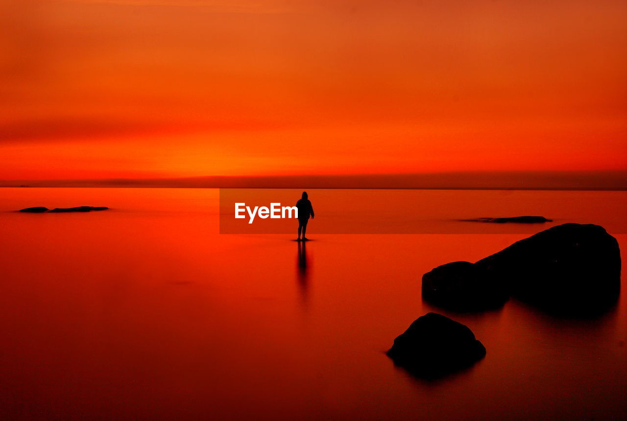 Rear view of woman standing on beach against sky during sunset