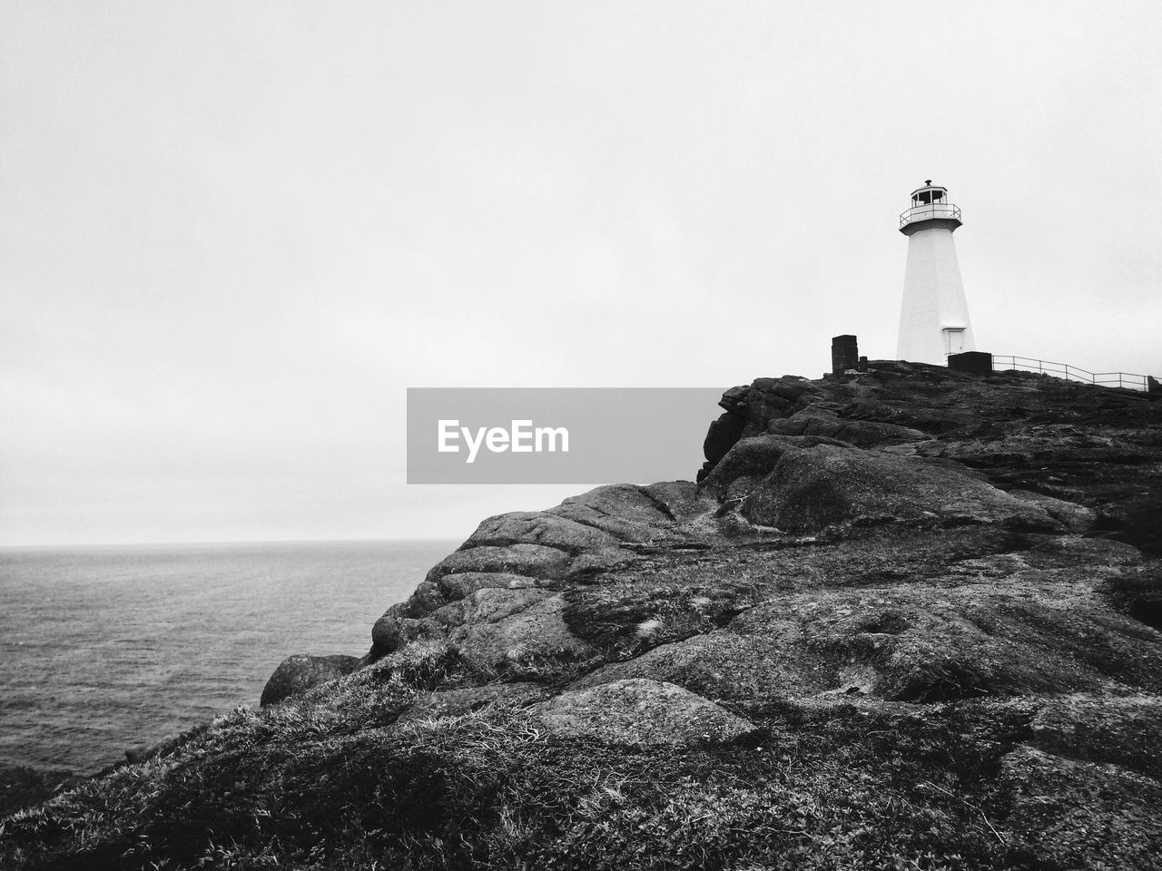 Lighthouse on cliff by sea against clear sky