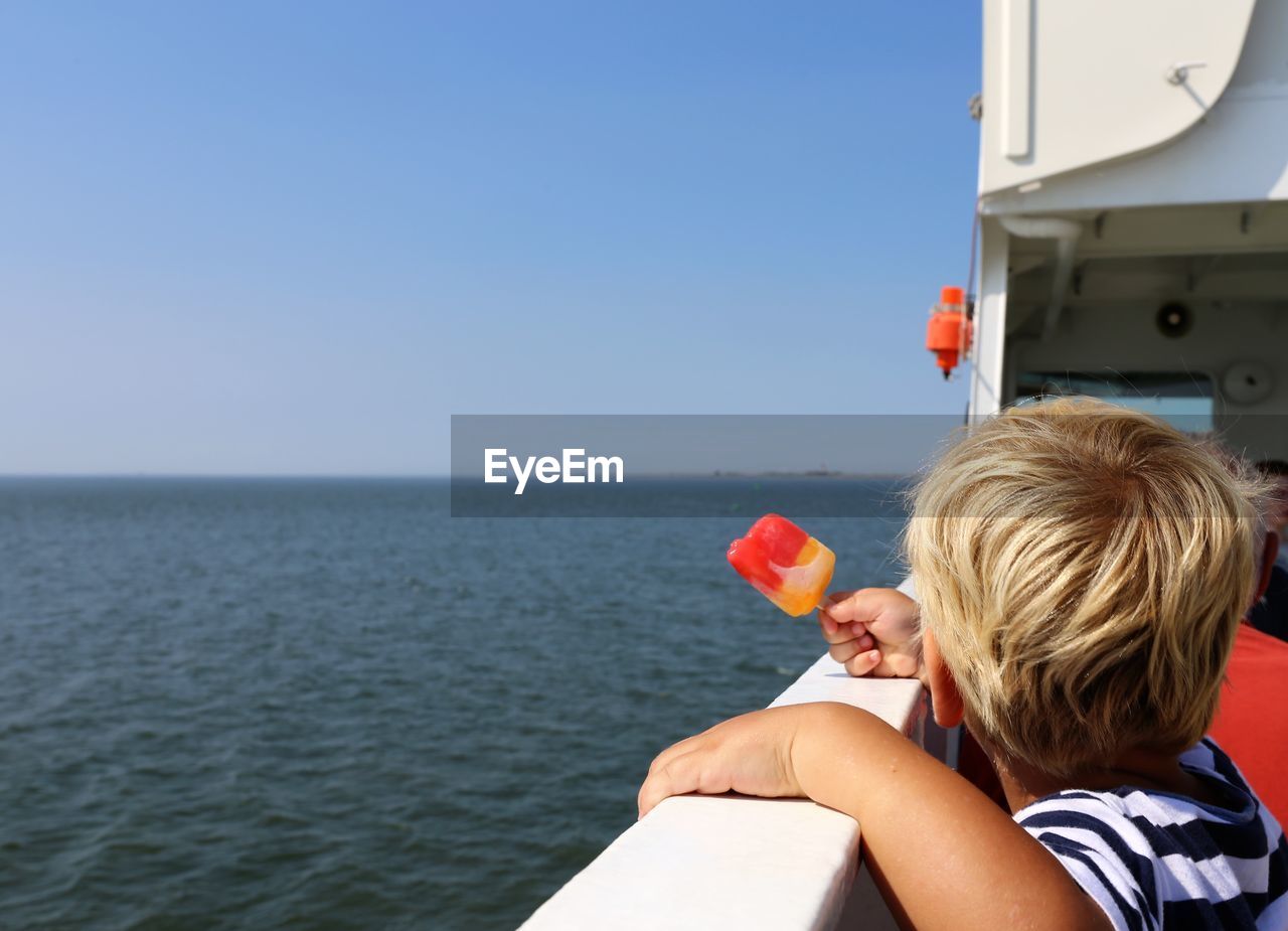 Toddler boy with popsicle on a ferry boat looking at distant island pellworm in the german north sea