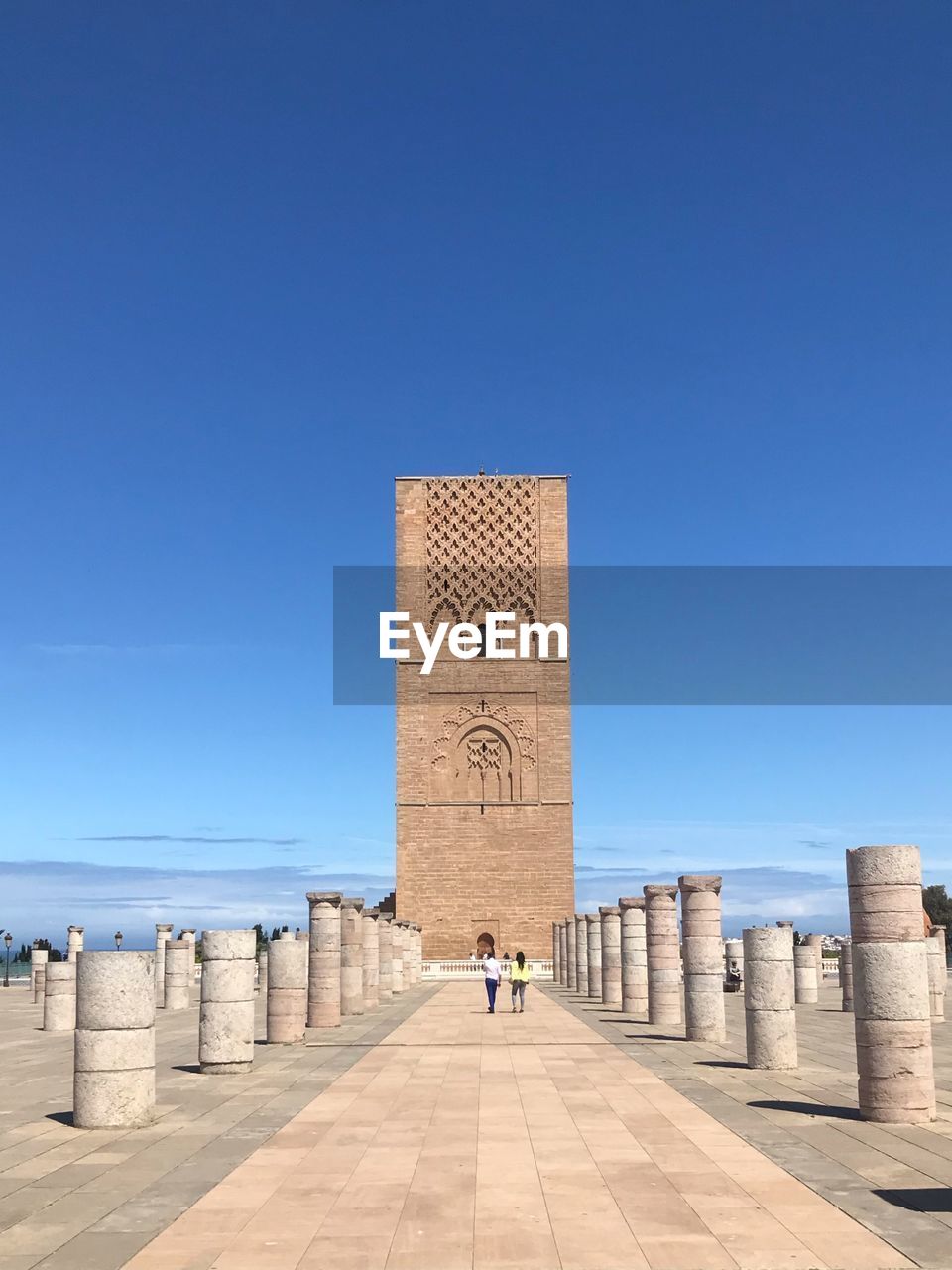 People walking towards historical building against clear blue sky