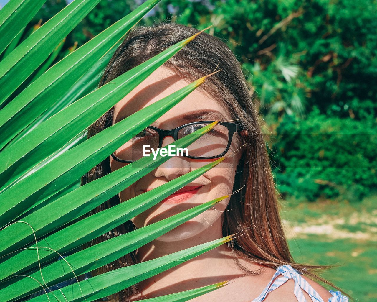 Portrait of young woman behind palm leaves