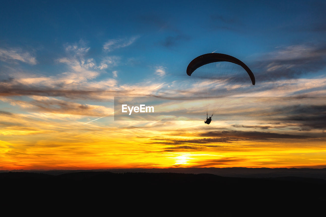 Silhouette person paragliding against sky during sunset