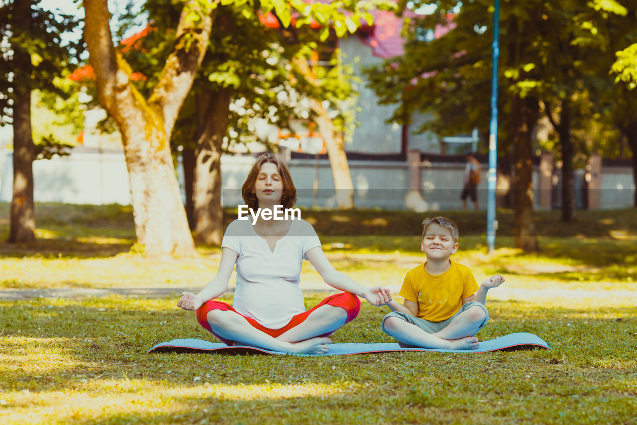 FULL LENGTH OF SMILING WOMAN SITTING ON GRASS IN PARK