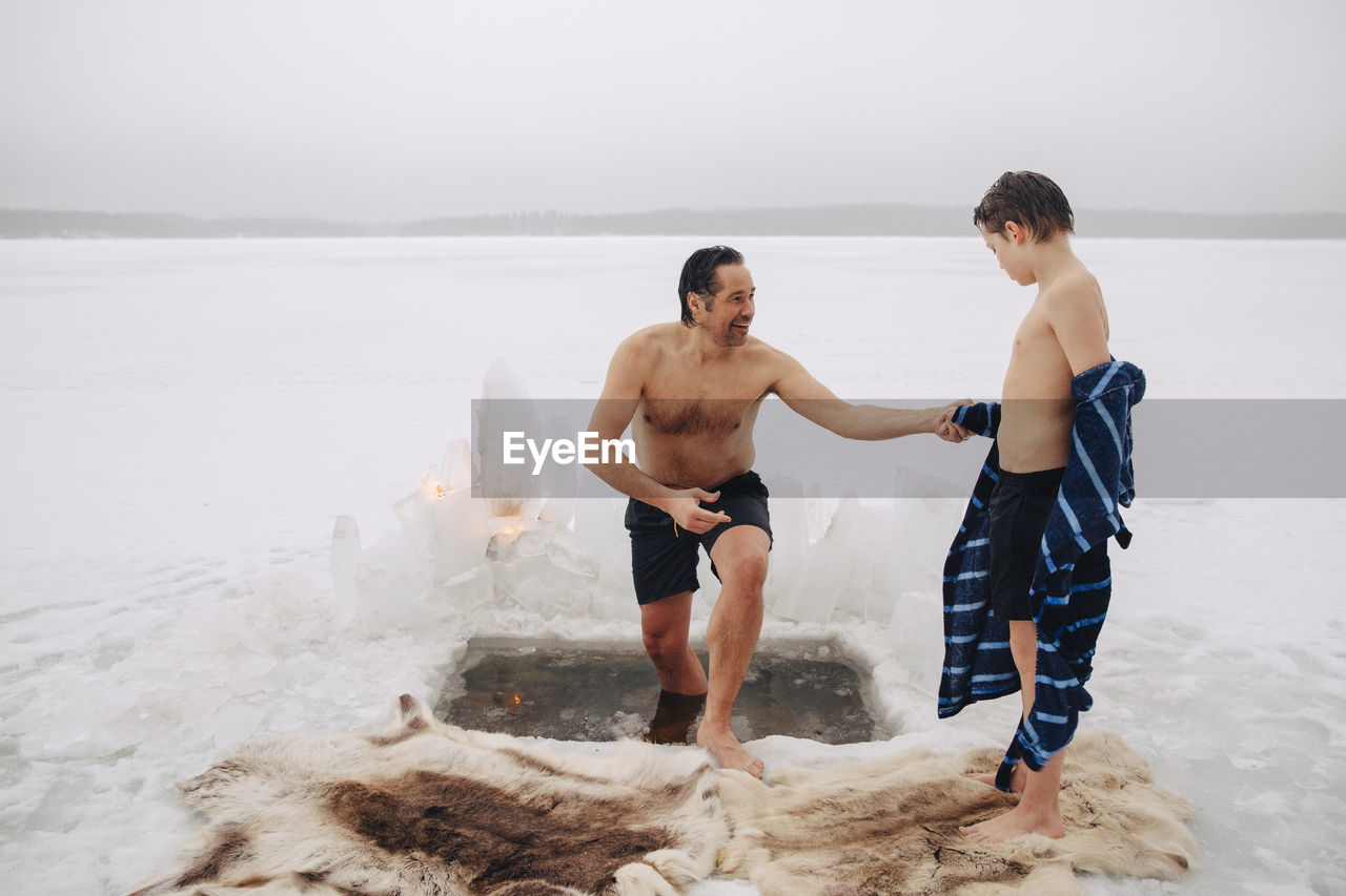 Smiling man holding son's hand while coming out from ice bath