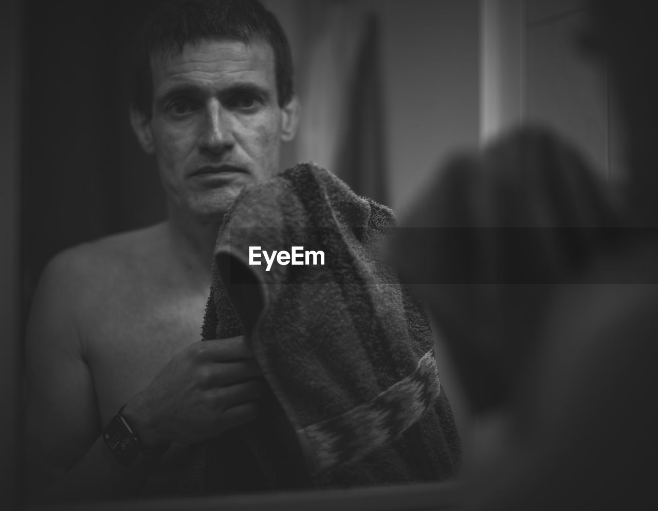 Portrait of young man at home in front of mirror holding towel