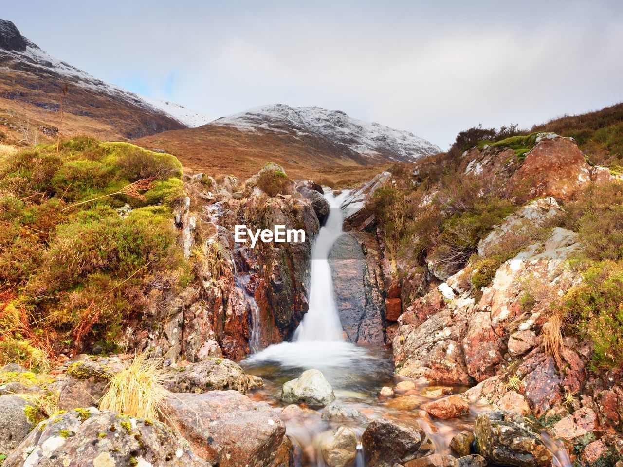 Rapids in small waterfall on stream, higland in scotland spring day. snowy cone of mountain