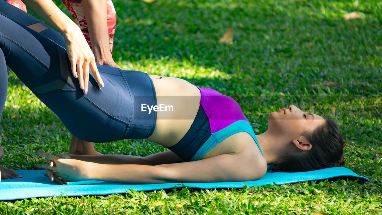 Yoga instructor assisting woman while exercising at park