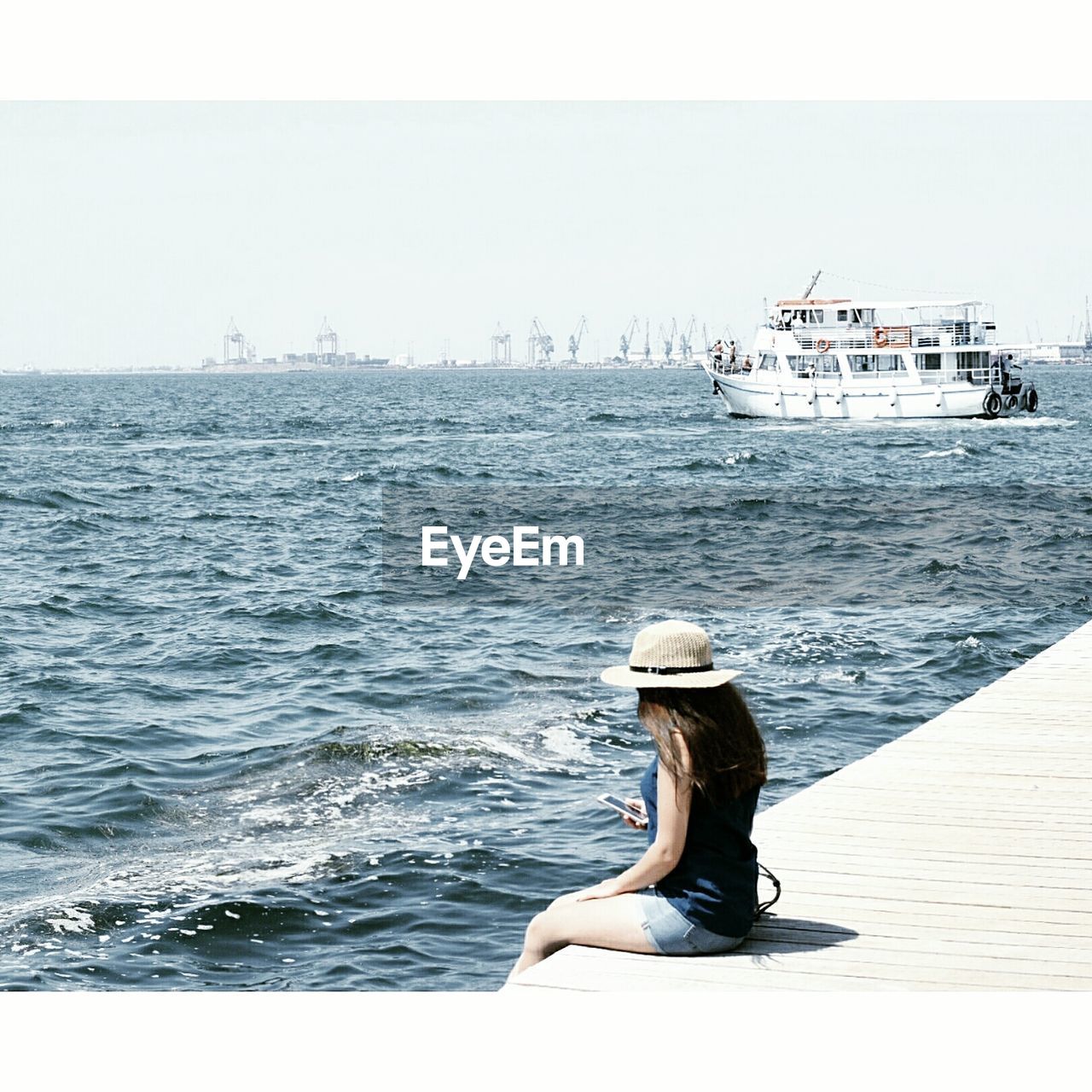 REAR VIEW OF WOMAN SITTING ON BOAT AGAINST SEA