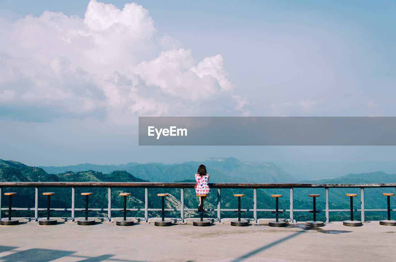 Woman sitting by railing against sky