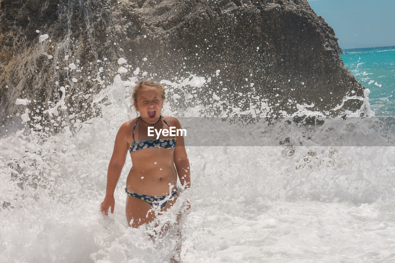 Girl wearing swimwear screaming while standing in wave
