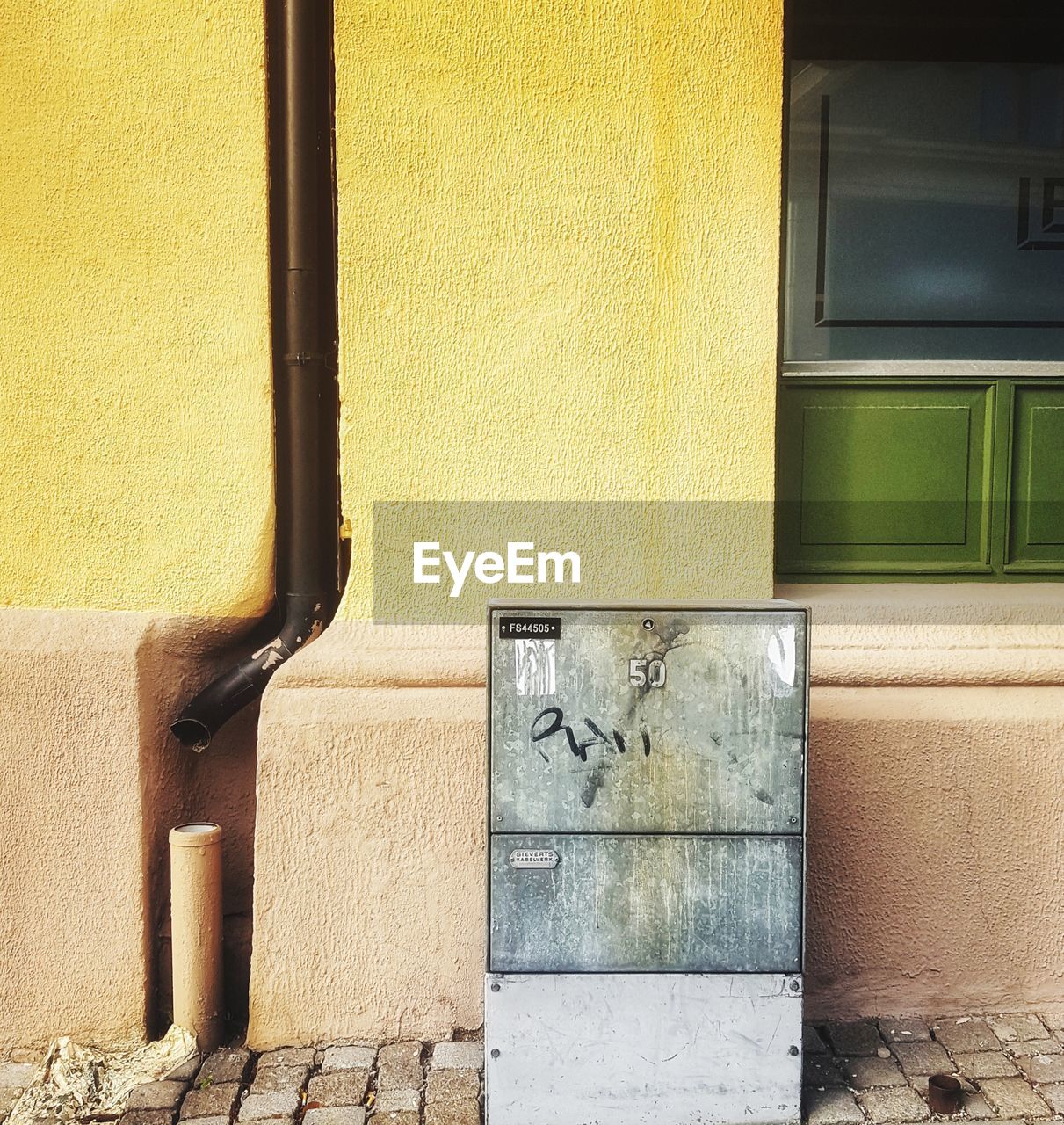 Drainpipe and fusebox against yellow wall