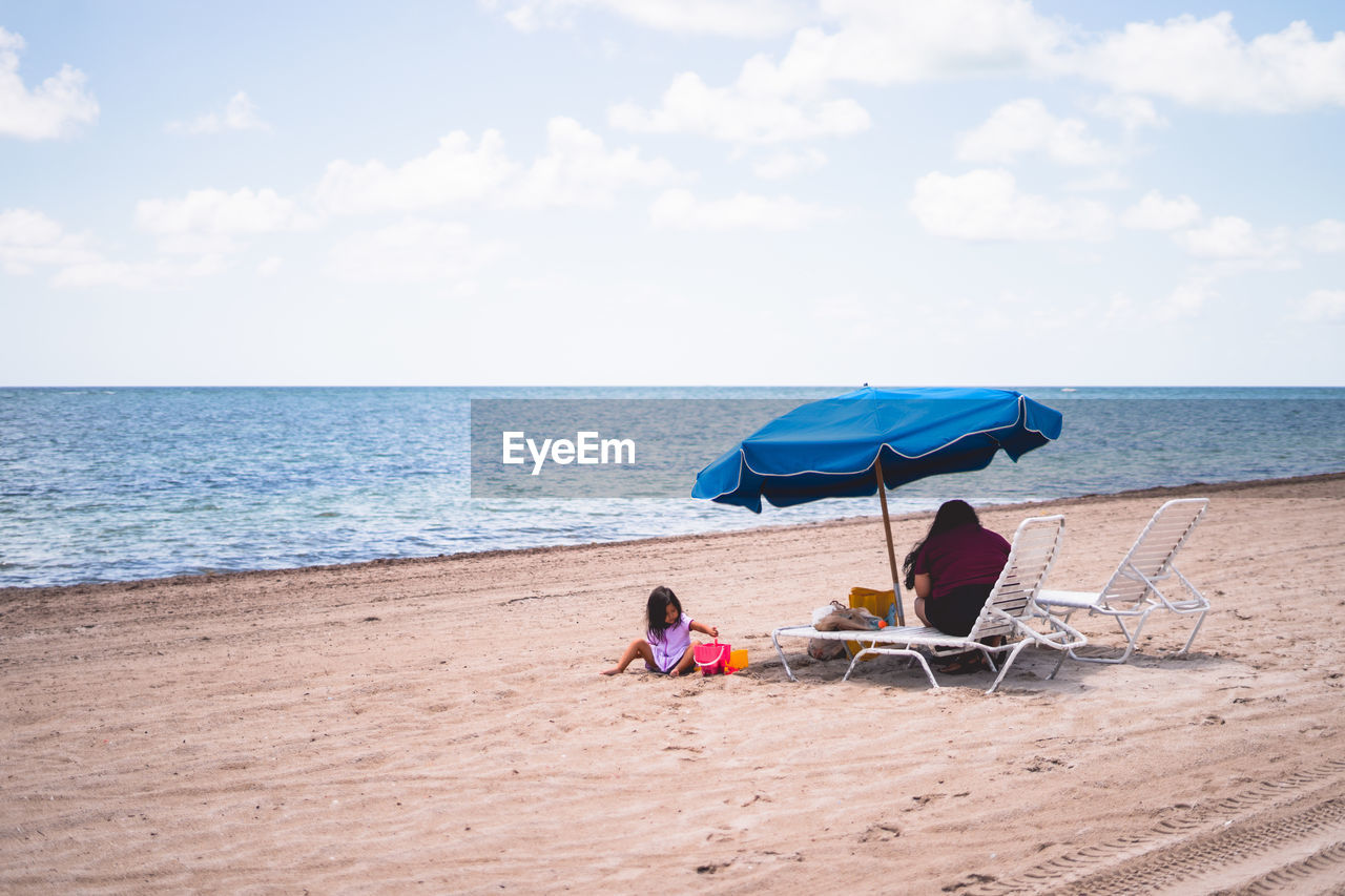 beach, water, sea, land, sky, horizon over water, shore, sand, horizon, vacation, trip, holiday, nature, ocean, body of water, cloud, chair, umbrella, relaxation, beauty in nature, summer, coast, adult, sitting, leisure activity, two people, men, scenics - nature, tranquility, day, togetherness, women, tranquil scene, protection, full length, seat, travel, lifestyles, travel destinations, weekend activities, outdoors, sunlight, rear view, idyllic, parasol, childhood, bay, copy space, blue, beach umbrella, enjoyment, shade, child, lounge chair, bonding, security, female, tourism
