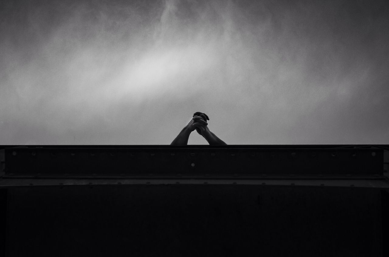 Hands clasped behind wall and against sky