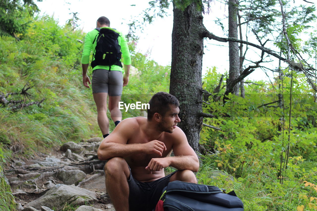 Shirtless young man sitting at forest