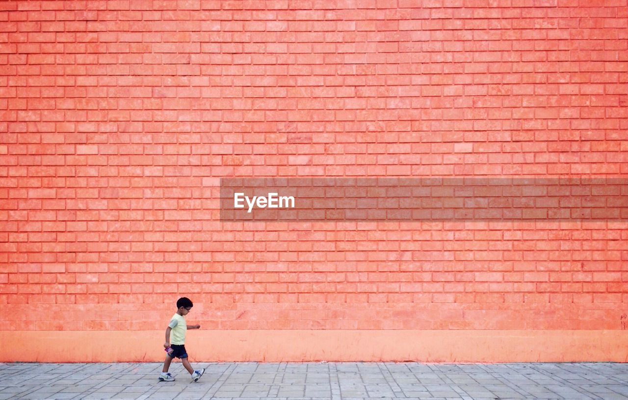 Full length of boy walking on sidewalk against wall