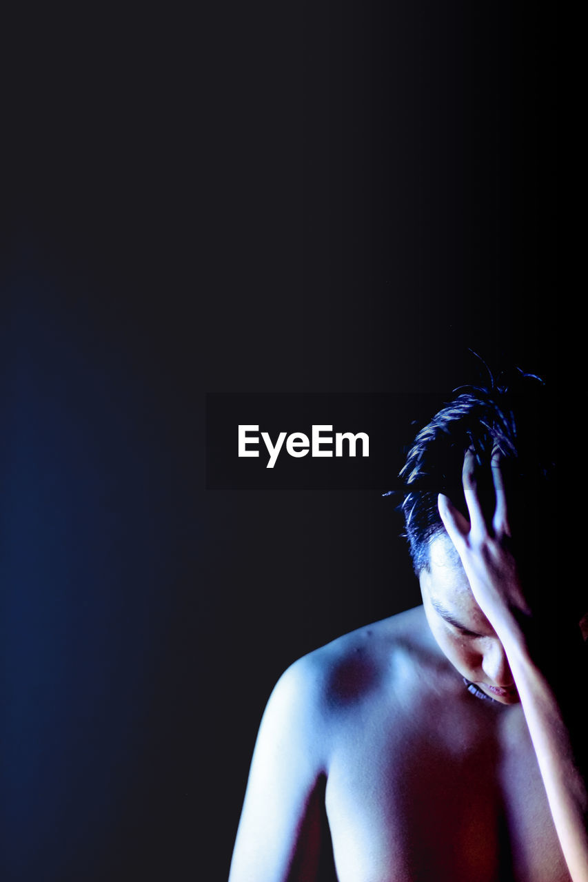 Young man with hand in hair standing against black background