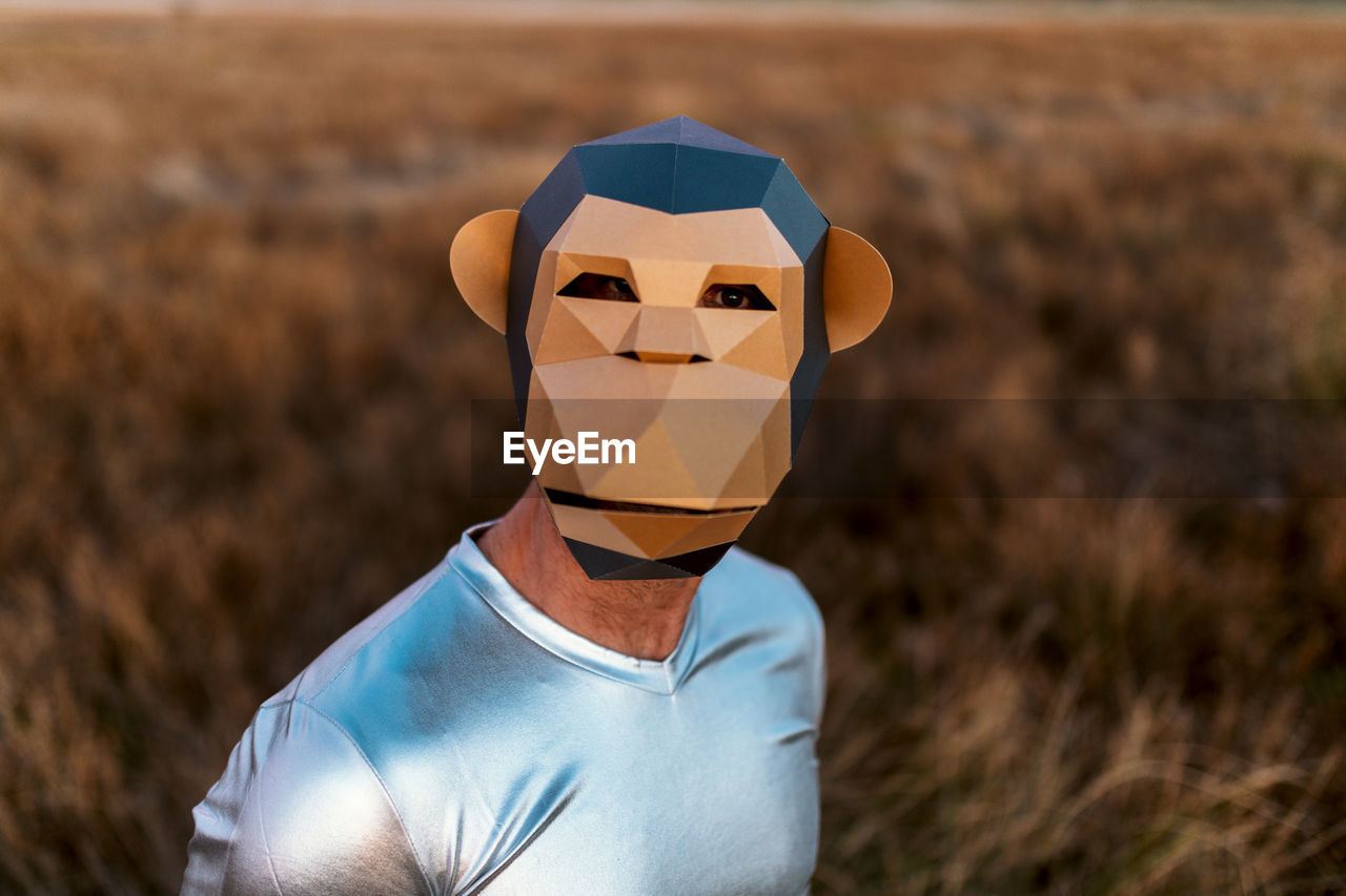 Anonymous person in geometric monkey mask looking at camera in yellow field on blurred background