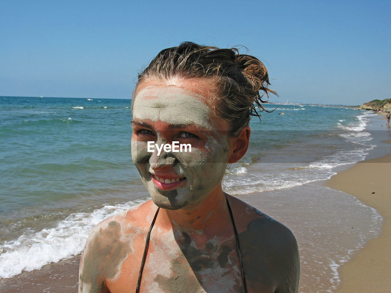 Portrait of woman wearing mud mask at beach against clear sky