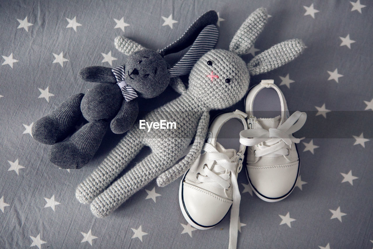 Two grey knitted toy rabbit and children's white shoes are on grey background with stars